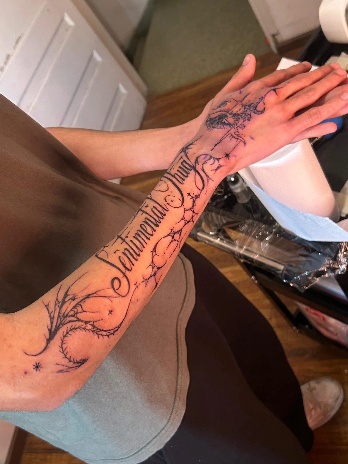 Lettering ornamental Sentimental Thug en el antebrazo, con elementos ilustrativos que llegan a la mano.