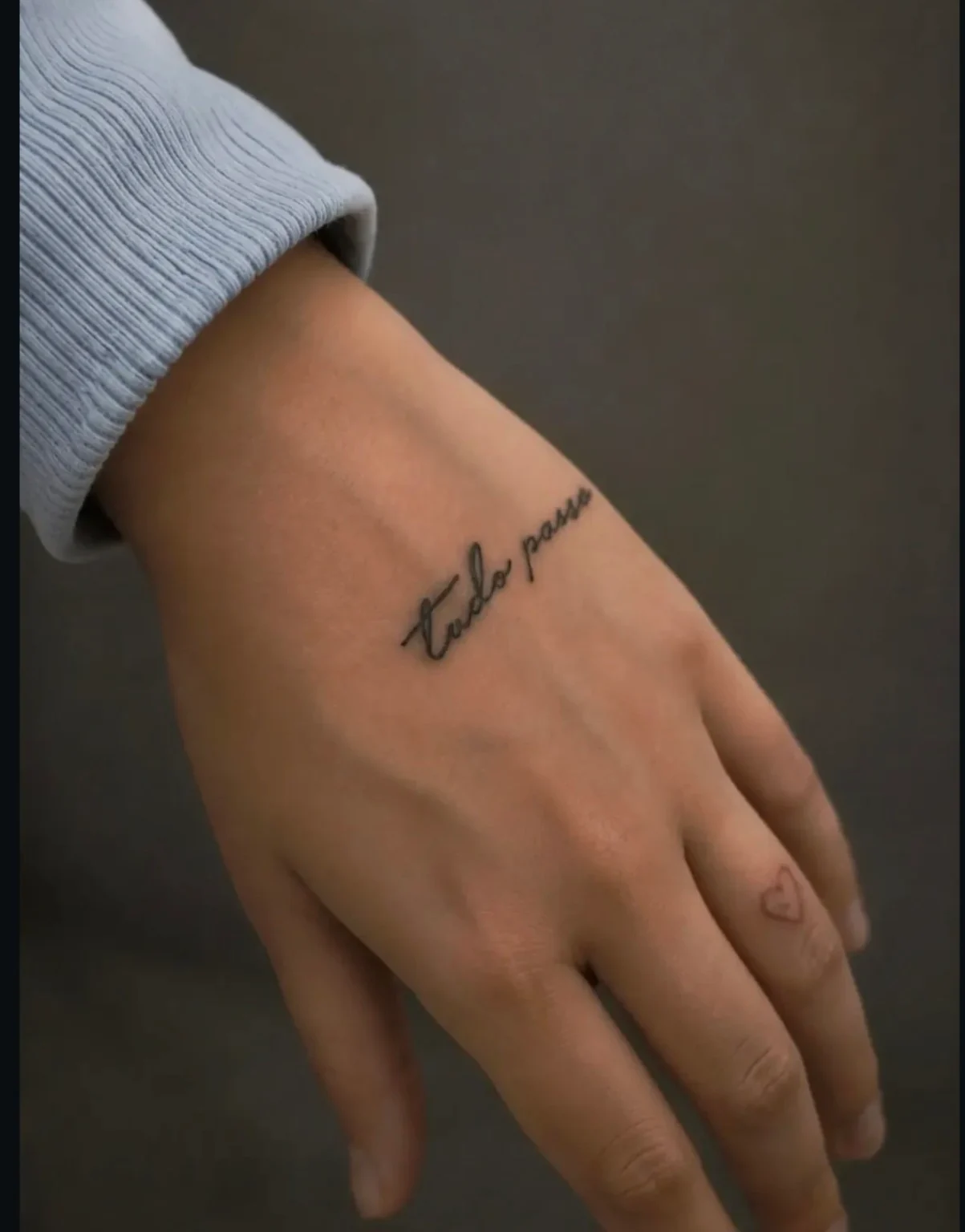 Frase en portugués Tudo passa en letra manuscrita sobre la mano.